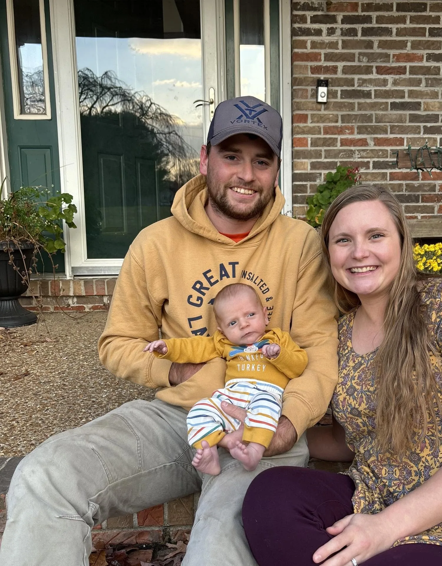 Jacob Doss, owner and licensed surveyor at Doss Land Surveying, seated on his front steps with his wife and infant son.