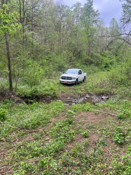 A Doss Land Surveying field truck parked at the end of a cleared corridor cut through wooded terrain.